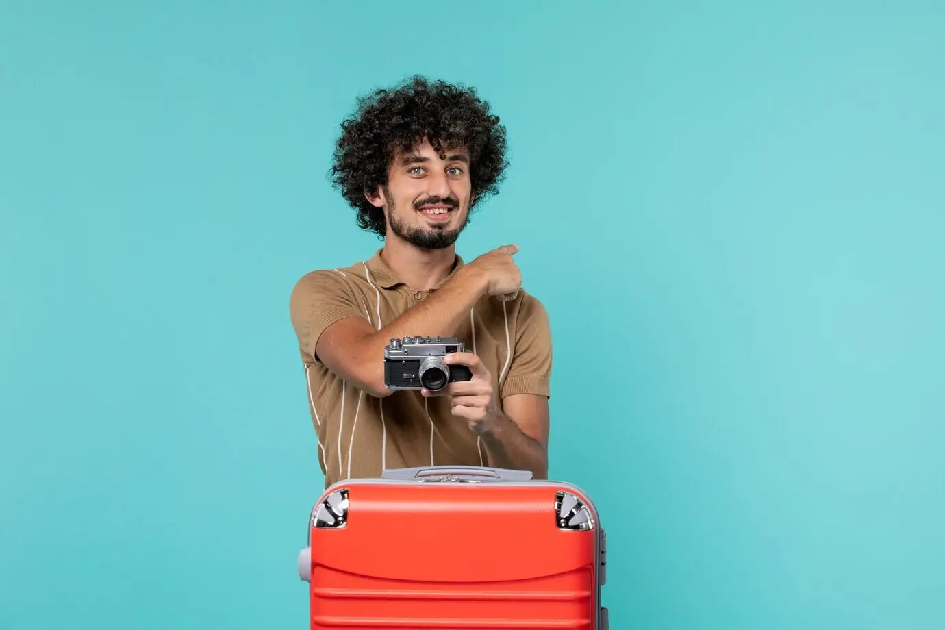 Mann im Urlaub mit großem rotem Koffer, der mit einer Kamera Fotos macht, vor blauem Hintergrund.
