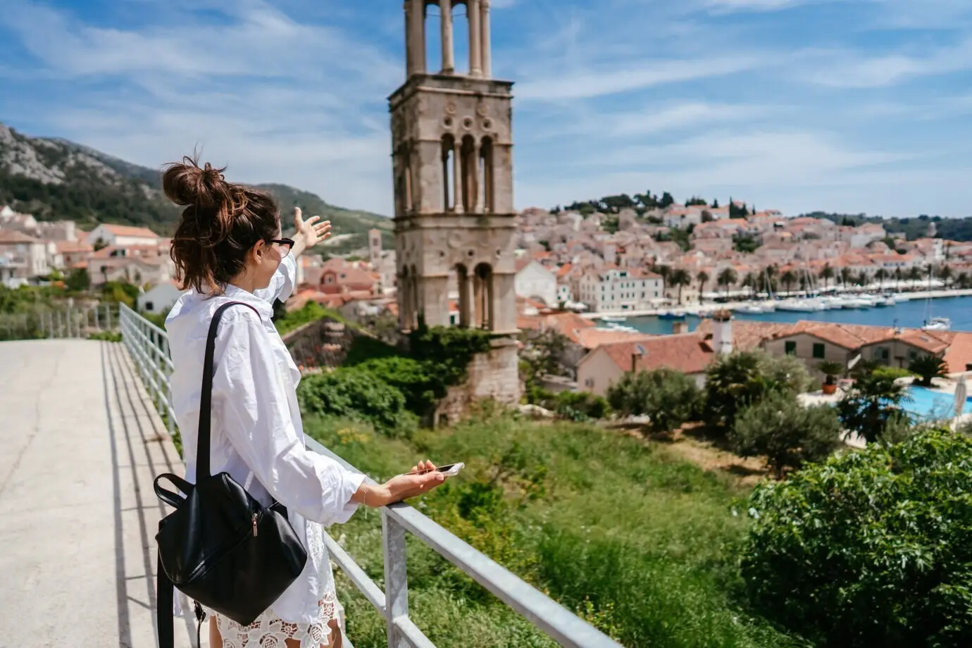 Junge, schöne Frau auf einem Balkon mit Aussicht auf eine kleine Stadt in Kroatien.